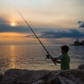 A young boy fishing in the setting sun at Piran Slovenia